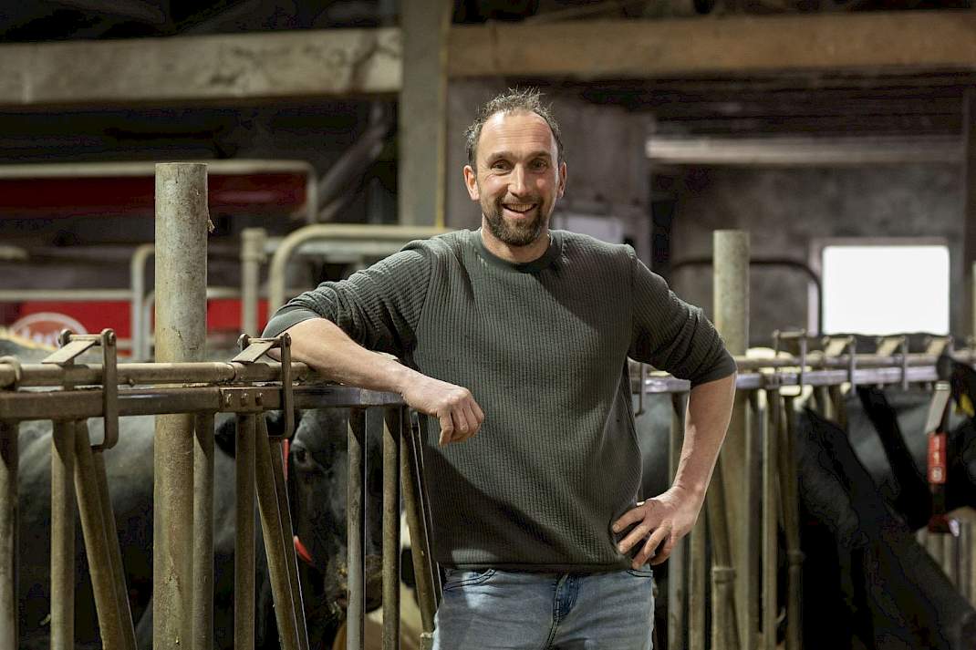 Melkveehouder in een koeienstal met een lely melkrobot op de achtergrond