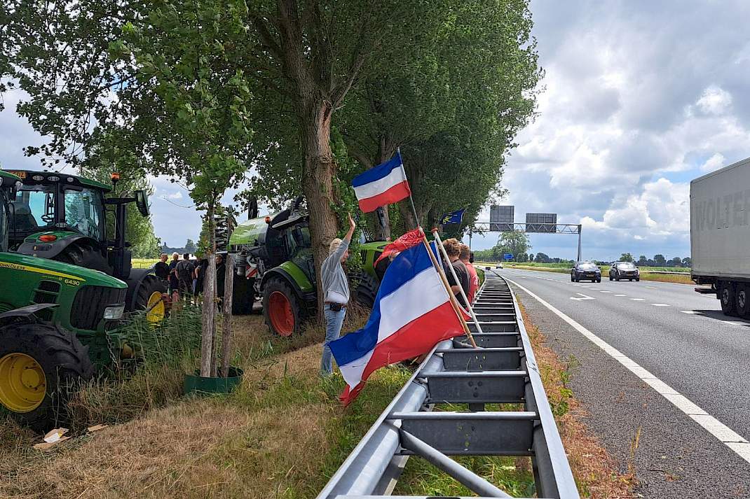 Boeren staan met trekkers en omgekeerde Nederlandse vlaggen langs de snelweg.