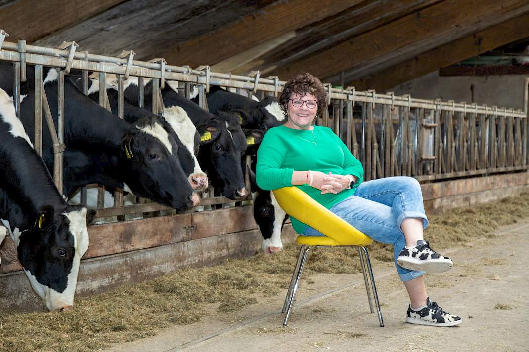 Ingrid de Sain zittend op een stoel op de voergang van een koeienstal