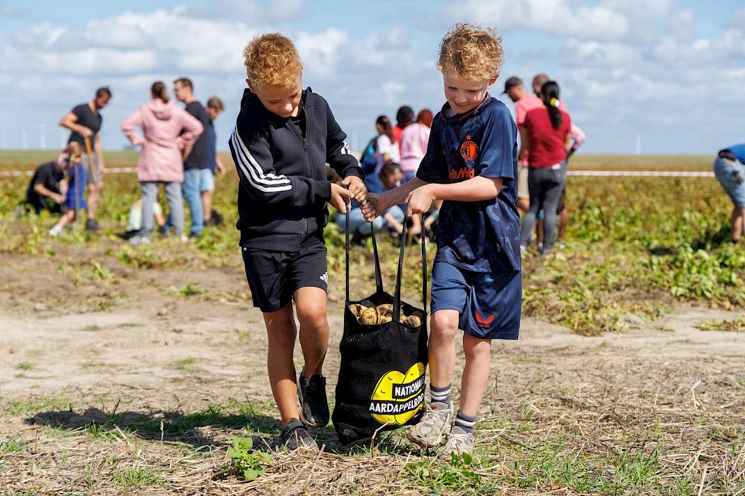 Twee kinderen sjouwen met een tas voor aardappelen